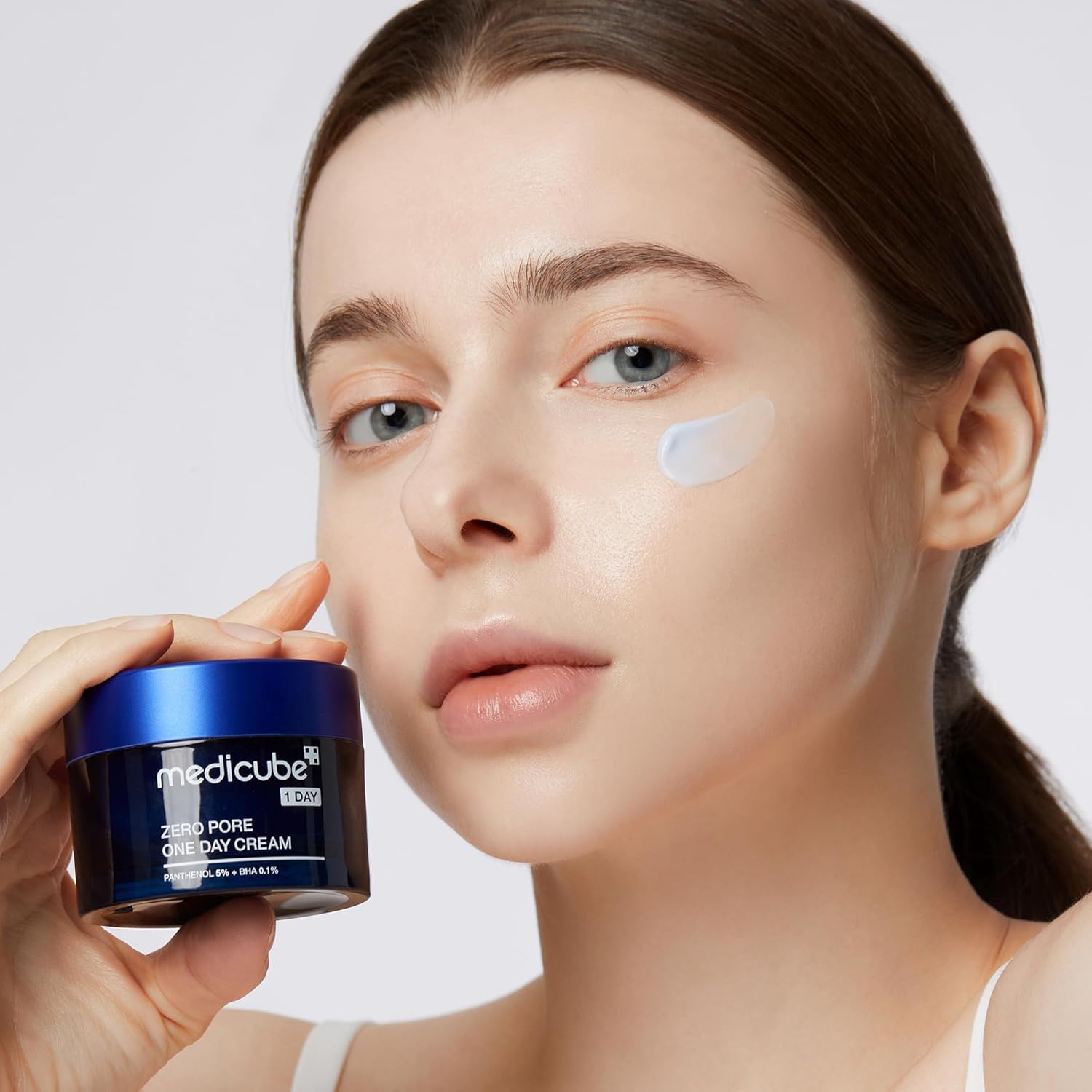 Woman holding a jar of Medicube cream with a white background